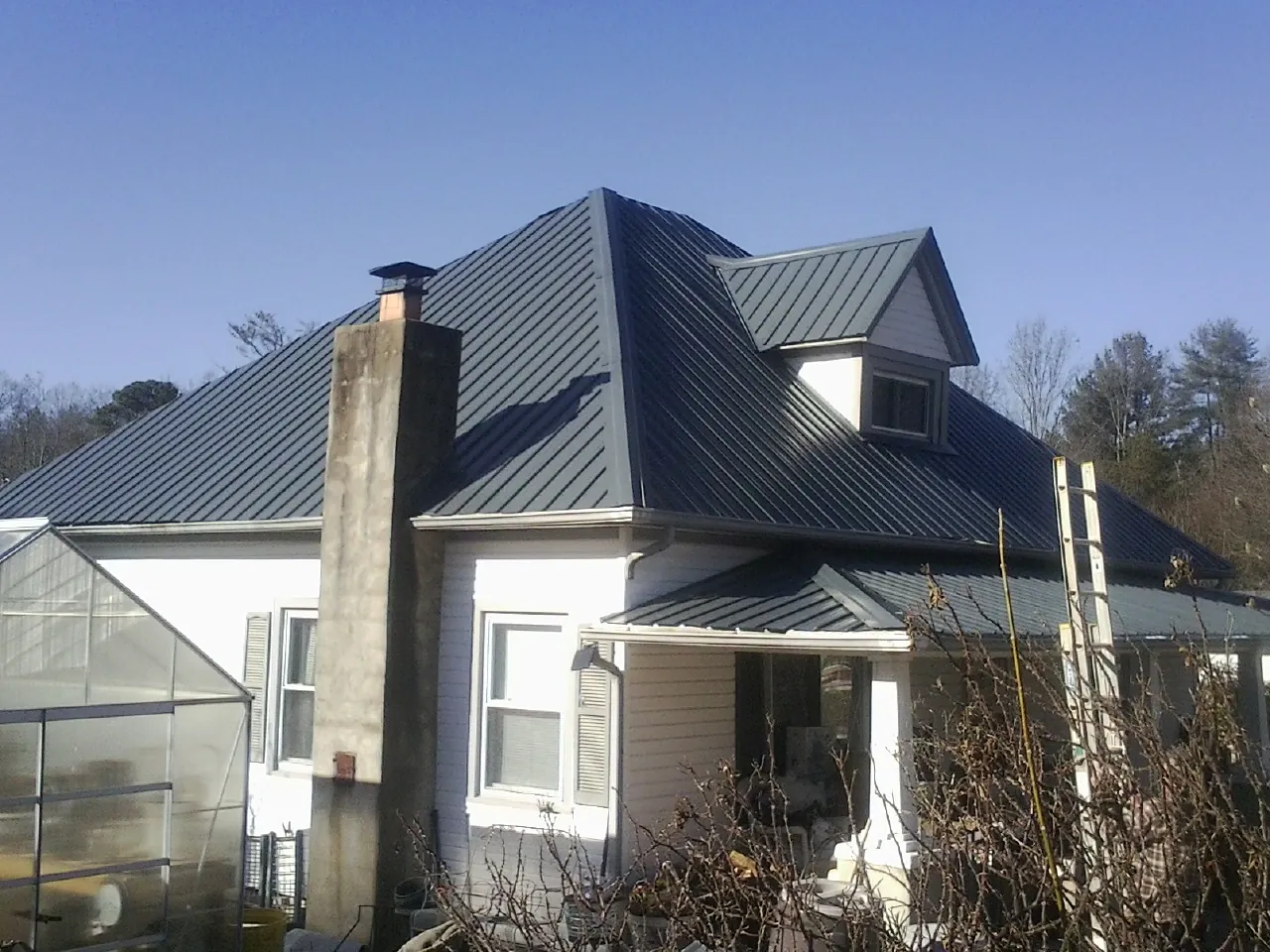 Dark blue standing seam metal roof on a white farmhouse with dormer in Adamstown