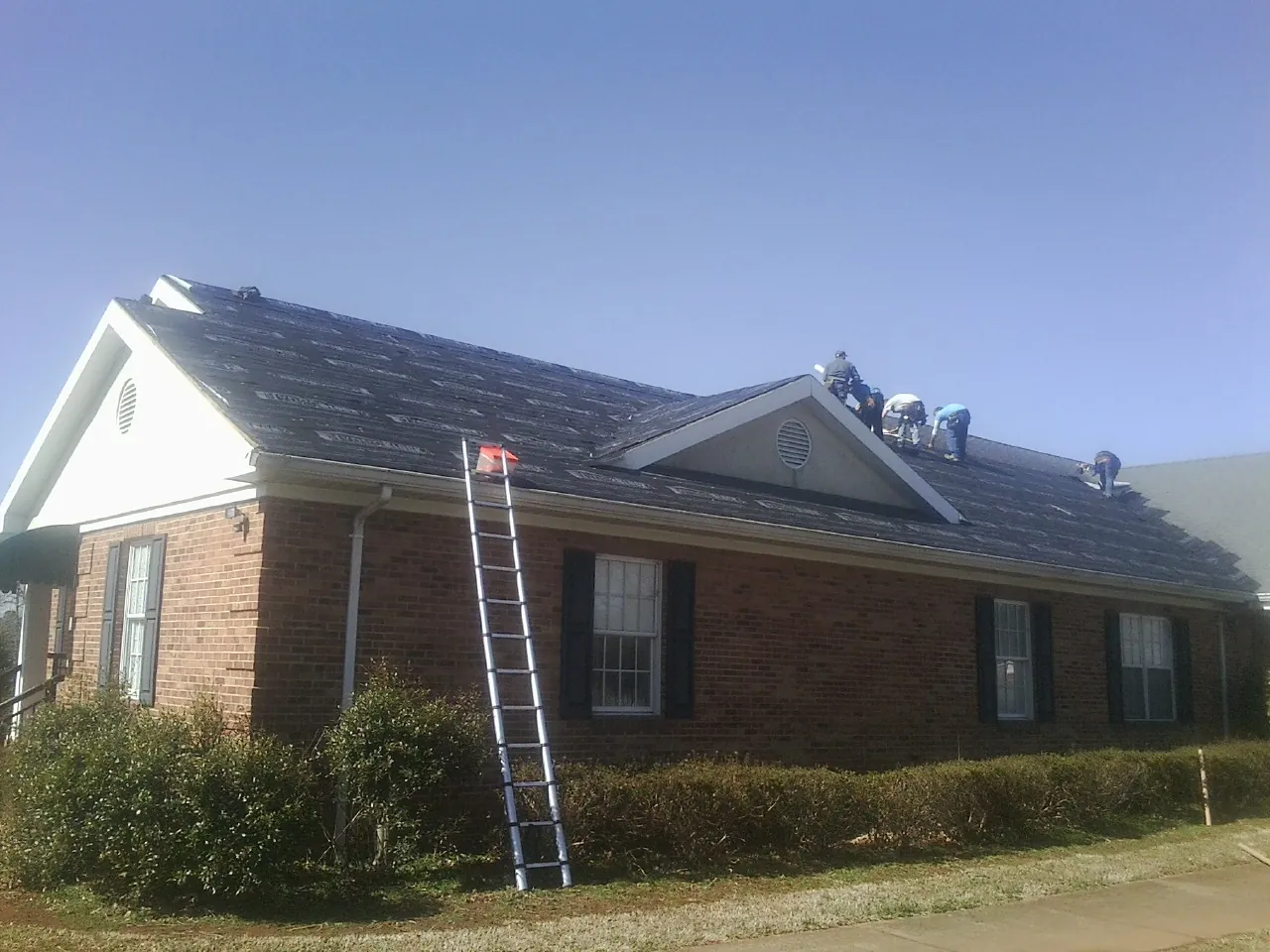 Crew tearing shingles off a brick ranch roof with a ladder set — Metal Roof Repair work by our crew in Adamstown