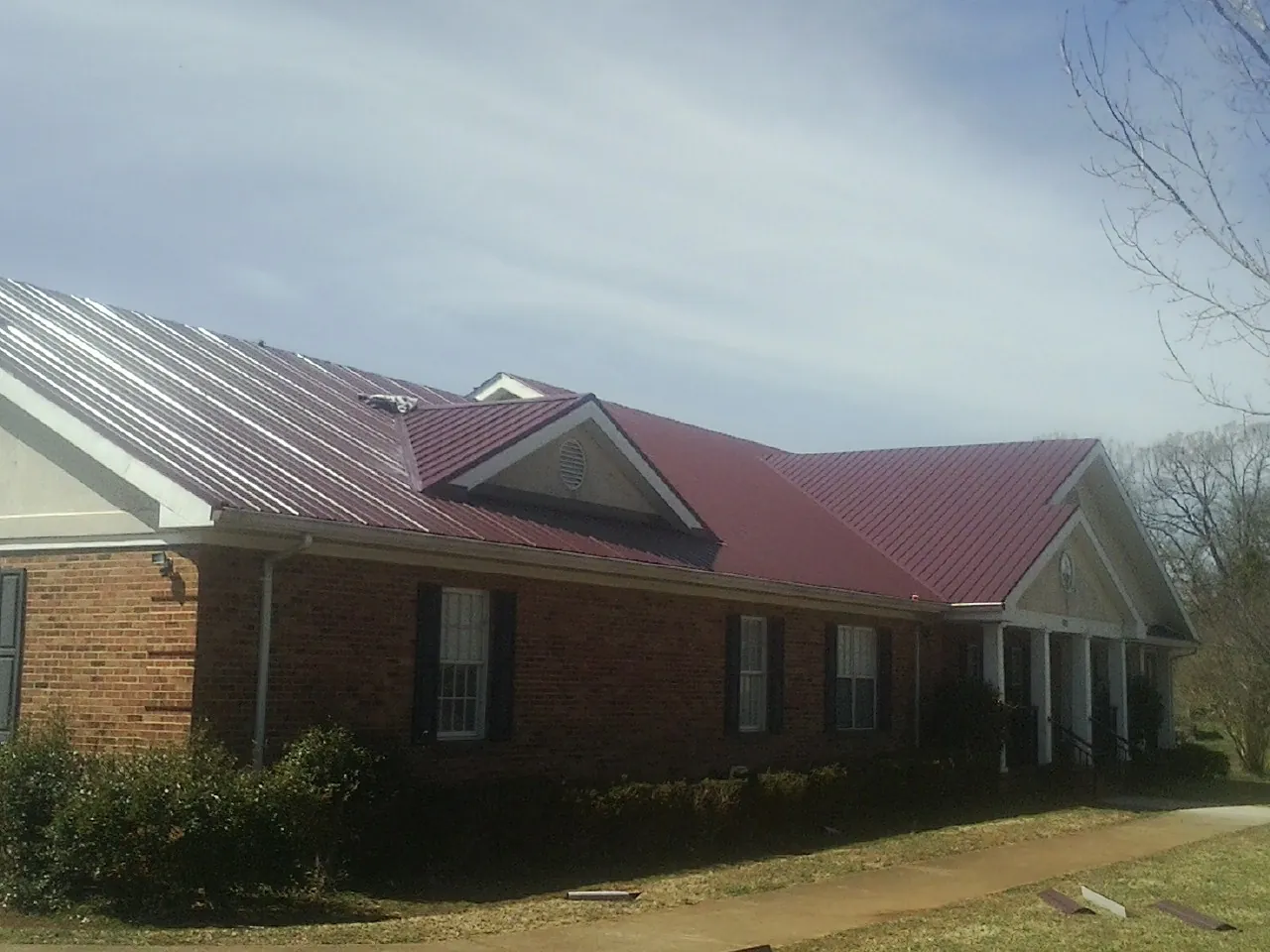 Red metal roof with gabled entries on a long brick building, from a Hail Damage Roof Repair job in Adamstown